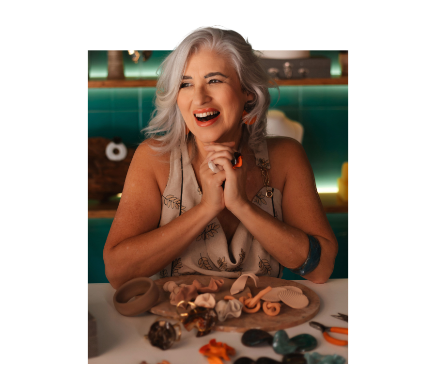 Márcia Campetti no ateliê sorrindo com as mãos na argila